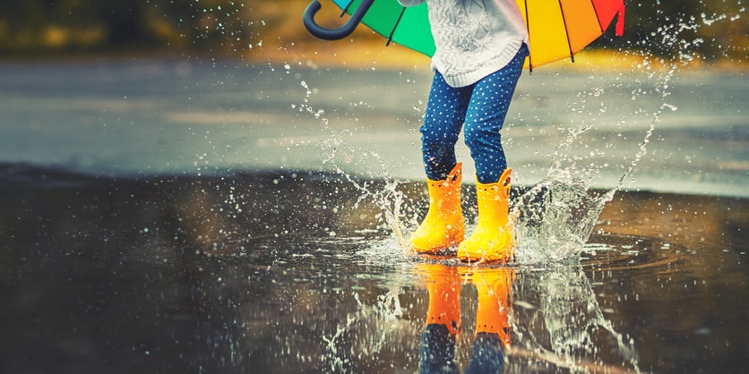 Feet of child in yellow rubber boots jumping over puddle in rain