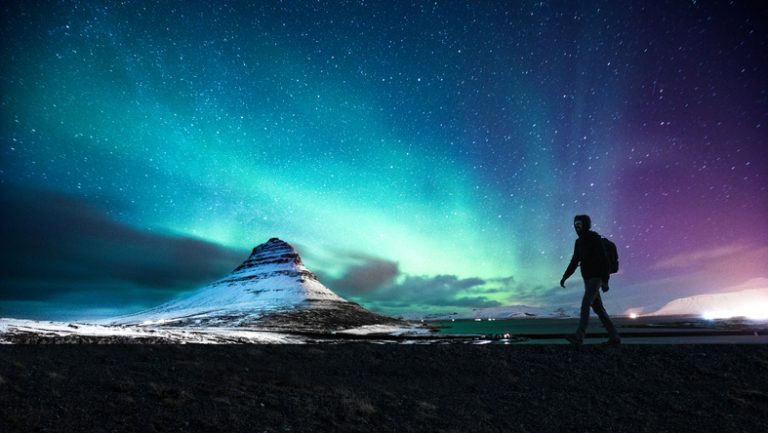 Northern lights in Mount Kirkjufell Iceland with a man passing by