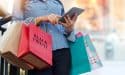 Woman using tablet and holding Black Friday shopping bag while standing on the stairs with the mall background