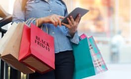 Woman using tablet and holding Black Friday shopping bag while standing on the stairs with the mall background